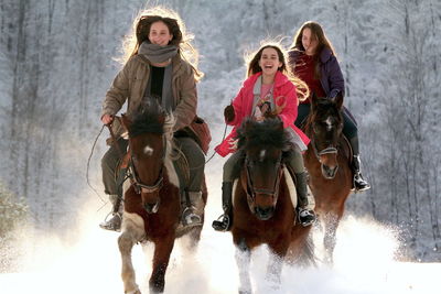 Full length of girls riding horses in snow covered land during winter
