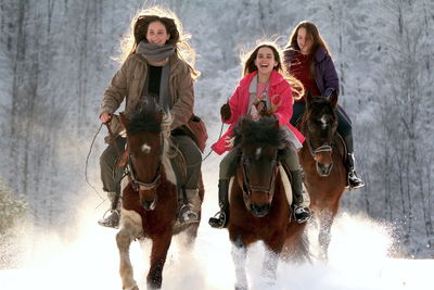 Full length of a young woman riding horse in winter