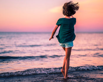 Rear view of man standing at beach during sunset