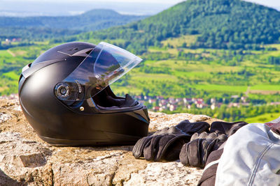 Close-up of helmet by gloves on retaining wall against mountains