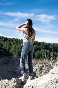 Rear view of young woman standing on rock against sky