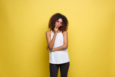 Portrait of young woman standing on yellow background