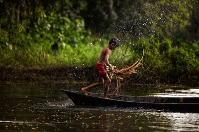 Side view of shirtless boy splashing water while on boat in river