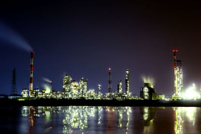 Reflection of illuminated factory on river against sky at night