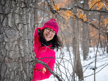 Happy woman standing by tree against snow