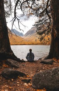 Rear view of woman sitting by lake against sky