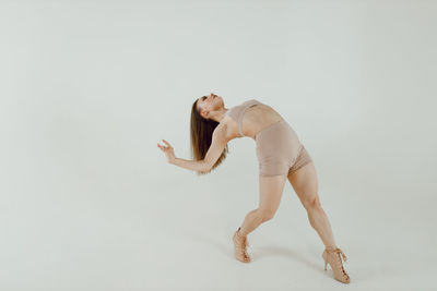 Low section of naked woman exercising against white background