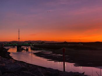 Silhouette bridge over river against sky during sunset