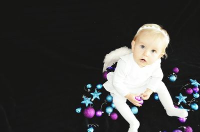 High angle portrait of baby girl in angel costume sitting amidst christmas ornaments