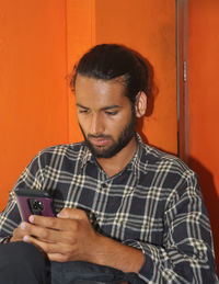 A bearded young guy with hair bun, using his phone while sitting indoors 