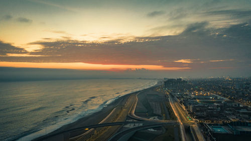 Aerial view of city by sea against sky at sunset