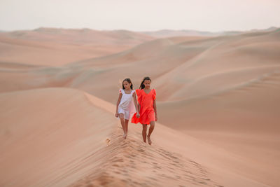 Sisters walking on sand dunes at desert