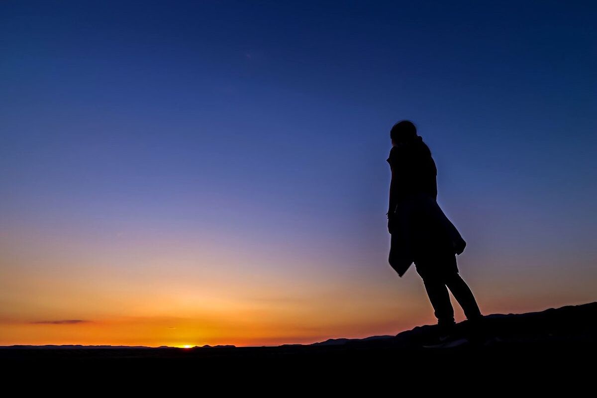 silhouette, sunset, clear sky, tranquil scene, standing, leisure activity, tranquility, scenics, carefree, nature, blue, sun, outline, getting away from it all, orange color, beauty in nature, mountain, outdoors, dark, solitude, mountain peak, calm, moody sky, cliff, romantic sky, escapism