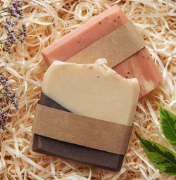 Assorted natural handmade soap bars and green leaves on a straw background
