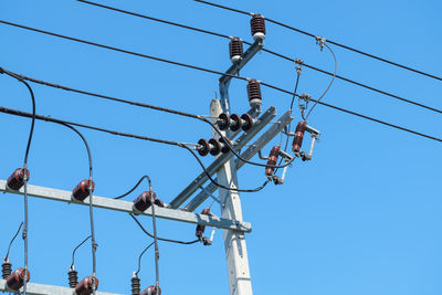 Low angle view of electricity pylon against blue sky