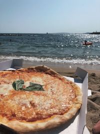 Close-up of pizza on table by sea against sky