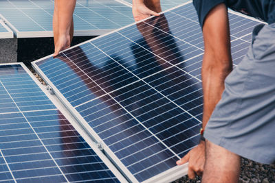 Cropped unrecognizable busy male engineers installing solar batteries in construction site of modern factory during sunny day