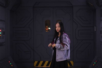 Portrait of young woman standing against door