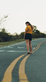 Rear view of man skateboarding on road against sky