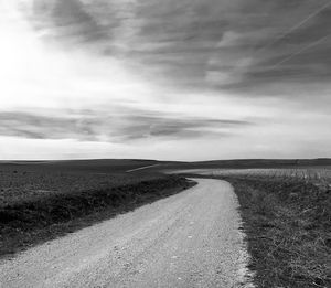 Dirt road on field against sky