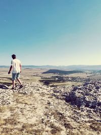 Man walking on rock against landscape and clear sky