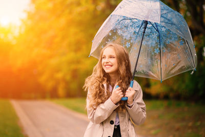 Portrait of young woman with umbrella standing against sky during sunset