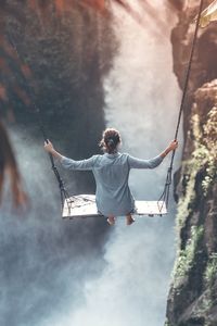 Rear view of woman on swing against waterfall