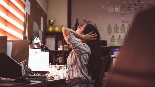 Side view of woman with hand in hair while working over computer at office