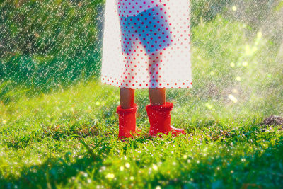 Low section of person wearing rubber boots and raincoat while standing on grass during rainfall