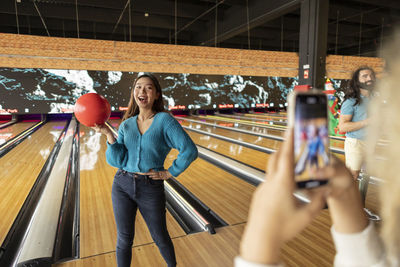 Woman photographing friend through smart phone in bowling alley