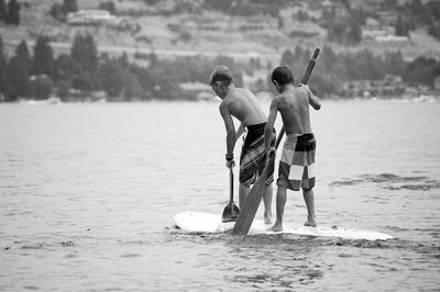 Rear view of boys paddleboarding on sea