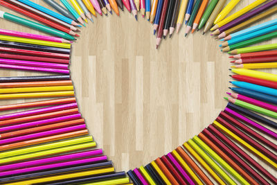 High angle view of multi colored pencils forming heart shape on table