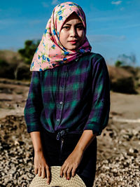 Portrait of young woman wearing hijab standing at beach