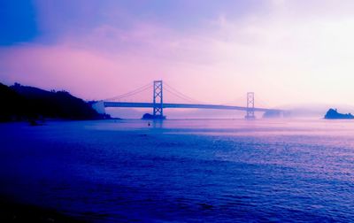 Suspension bridge over sea against sky during sunset