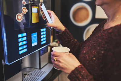 Woman paying for product at vending machine using contactless method of payment with mobile phone