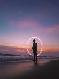 Digital composite image of man standing against circle on beach during sunset
