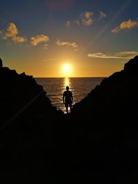 Silhouette man standing by sea during sunset