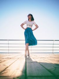 Low angle view of fashionable woman standing with hands on hip at boat deck against sky
