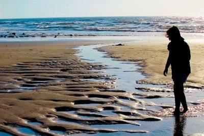 Rear view of woman standing at beach against sky