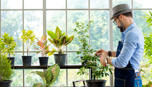 Man standing by potted plants against window