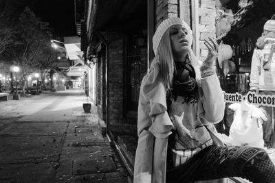 Woman smoking cigarette by store window in city