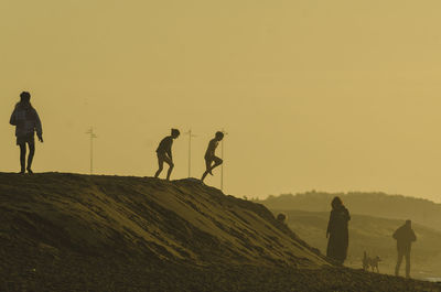 Silhouette people walking on desert against clear sky