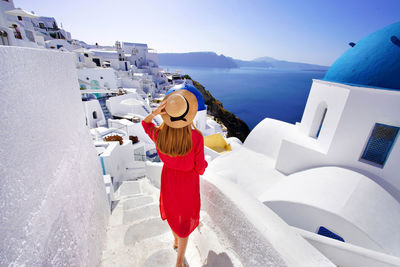 Girl in red dress and hat comes down the stairs oia village with view of the caldera, santorini
