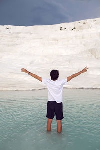 Man with a beard in a white t-shirt and shorts stand on a white mountain in pamukkale