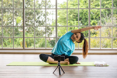 Smiling asian yoga coach stretch arms. film vlog by phone at home
