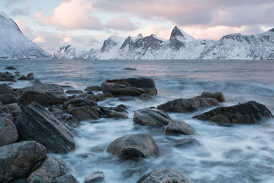 Scenic view of sea by snowcapped mountains against sky