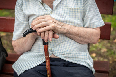 Midsection of senior man with walking cane sitting on bench