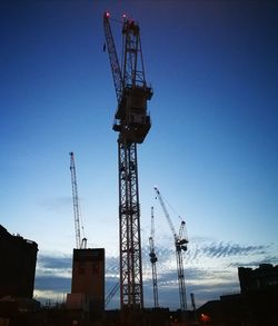 Low angle view of cranes at construction site against sky