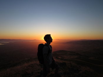 Silhouette of woman standing on landscape at sunset