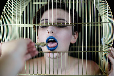 Cropped hand feeding food to woman in cage